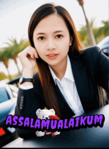 a woman in a suit holds a teddy bear in front of a sign that says assalaamualaikum