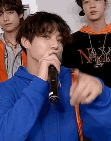 a young man in a blue hoodie is holding a microphone and pointing at something .