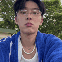 a young man wearing glasses and a pearl necklace is taking a picture of himself