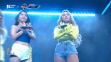 a woman in a neon yellow top stands on a stage in front of a screen that says 2019
