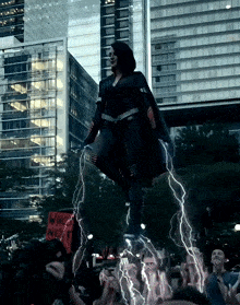 a woman in a black cape is surrounded by lightning while holding a sign that says who next