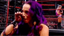a female wrestler with purple hair is crying in a ring .