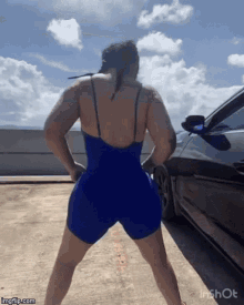 a woman in a blue bodysuit is dancing in front of a car