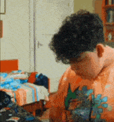 a boy with curly hair is wearing an orange shirt with a dinosaur on the back