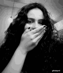 a black and white photo of a woman covering her face with her hands .