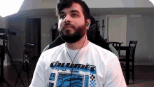 a man with a beard is wearing a white shirt with the word volumes on it