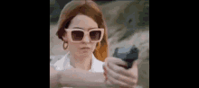a woman wearing sunglasses is holding a gun in her hand and pointing it at the camera .