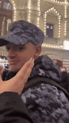 a man in a camouflage hat is being touched by a woman 's hand
