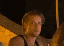 a man in a tank top is holding a glass of wine .