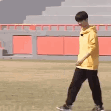 a young man wearing a yellow hoodie and black pants is walking on a field .