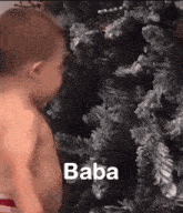 a baby is standing in front of a christmas tree with the word baba written on it .