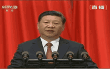 a man in a suit and tie is giving a speech in front of microphones with cctv 13 written on the screen behind him