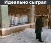 a man with a cane is walking down a snowy street in front of a fence