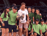 a man holding a trophy is surrounded by a group of people wearing green lacoste shirts