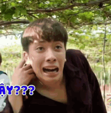a young man is making a funny face with the words " why ?? " behind him .