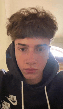 a young man with a nose ring is wearing a hoodie and looking at the camera .