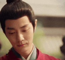a man with his hair in a bun is wearing a red jacket
