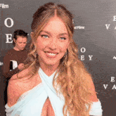 a woman in a blue dress smiles in front of a sign that says " film "