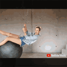 a woman is hanging from a chain on a ball with youtube music written on the bottom