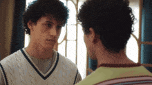two young men are looking at each other and one is wearing a sweater vest