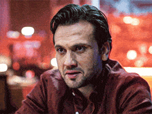 a man with a beard wearing a red shirt is looking at the camera