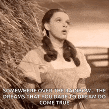 a black and white photo of dorothy from the wizard of oz standing next to a haystack .