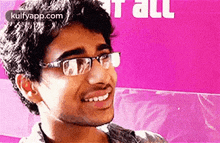 a young man wearing glasses is smiling in front of a pink sign .