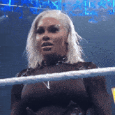 a woman with blonde hair is standing in a wrestling ring with the letter v on her chest