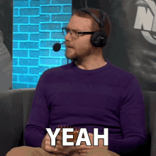a man wearing headphones and a purple sweater says " yeah "