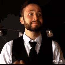 a man with a beard is wearing a vest and tie and making a funny face .