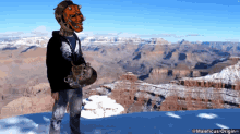 a man wearing a mask stands on top of a snow covered mountain