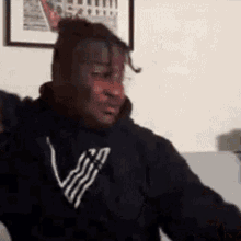 a man is sitting on a couch wearing a black hoodie with the letter v on it .