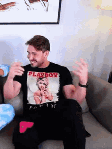 a man is sitting on a couch wearing a black playboy shirt