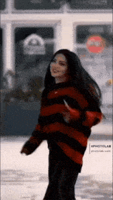 a woman wearing a red and black striped sweater is standing in front of a building .