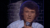 a man singing into a microphone with a brick wall behind him