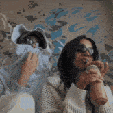 a woman drinking a smoothie with a straw while another woman covers her face with a hoodie