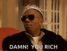 a man wearing a crown and sunglasses is sitting on a couch and saying `` damn you rich '' .