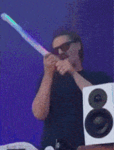 a man wearing sunglasses and a hat is standing in front of a speaker with his arms in the air
