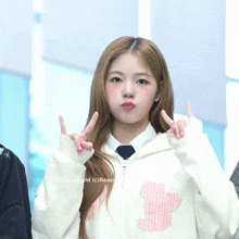a girl wearing a white sweatshirt with a pink bear on it making a peace sign