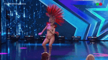 a woman in a feathered costume is dancing on a stage in front of a screen that says #gotalentargentina