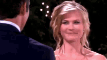a man and a woman are looking at each other and smiling . the woman is wearing a wedding dress .