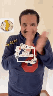 a man wearing a blue hoodie with a happy anniversary sticker on it is clapping .