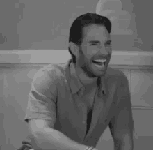 a black and white photo of a man laughing while sitting at a table .