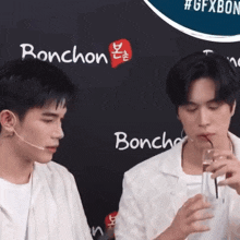 two men drinking from glasses with a straw in front of a sign that says bonchon