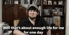 a man is sitting at a desk in front of a bookshelf and talking about enough life for one day .