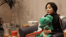 a woman is sitting on a couch holding a green stuffed dinosaur