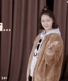 a woman wearing a fur coat and a hoodie is giving a peace sign .
