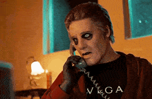 a man wearing a black shirt that says vega on it is talking on a phone