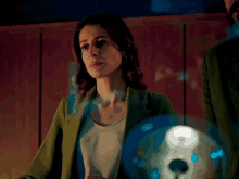 a woman in a green jacket is standing in front of a glowing object