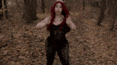 a woman with red hair is standing in the woods wearing a black bodysuit